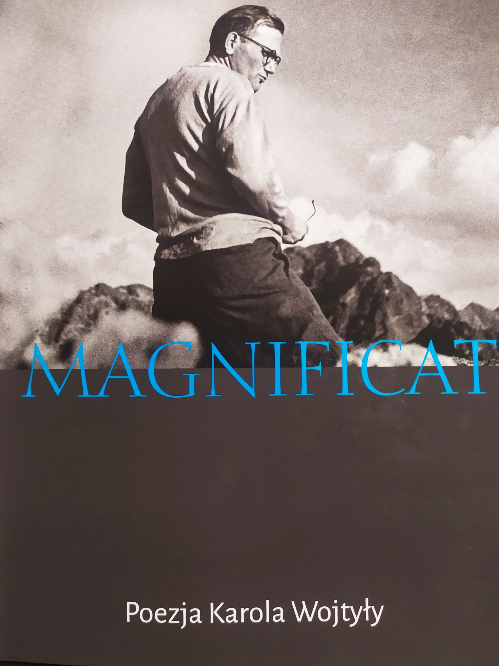 Mężczyzna w okularach. Widoczny napis - niebieskimi literami - Magnificat