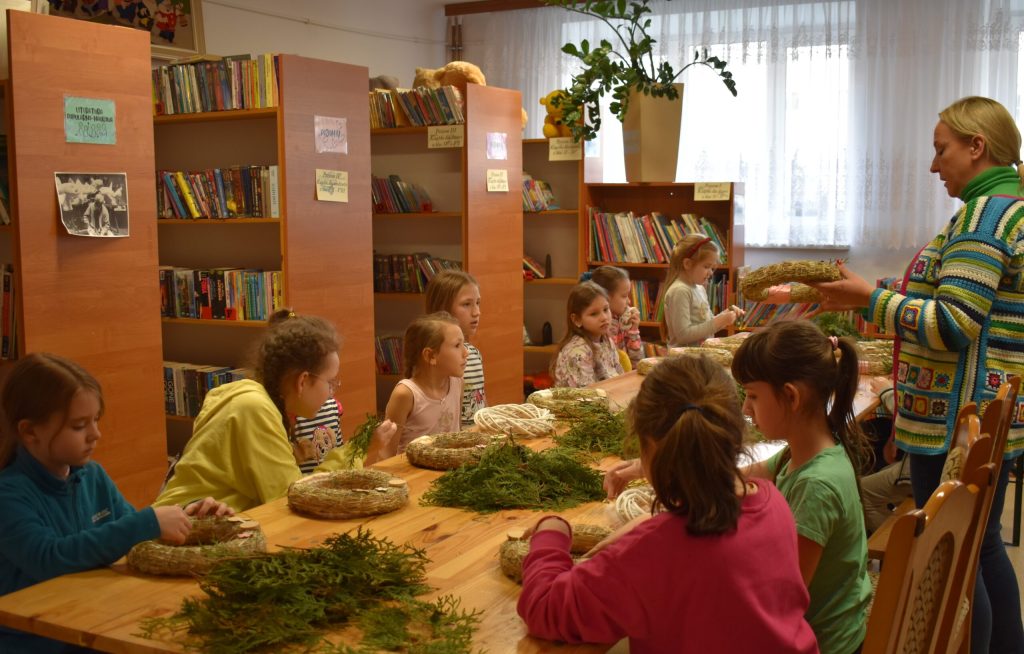Na dzieciach udział w warsztatach plastikowych w bibliotece, pod kierunkiem instruktora. Młodzi twórcy są skupieni na swoich projektach, a nauczyciel znajduje się w czymś, co jest dostarczane.